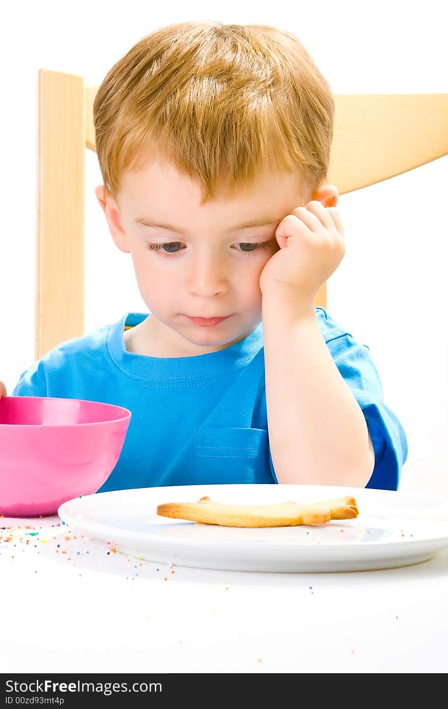 A moodly three year old in a blue top with a biscuit and sweets and a day dreaming expression. A moodly three year old in a blue top with a biscuit and sweets and a day dreaming expression