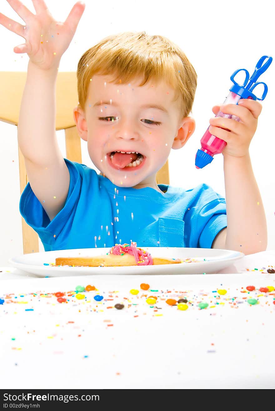 Three year old boy in blue top decorating biscuits with pink icing and sweets. Three year old boy in blue top decorating biscuits with pink icing and sweets