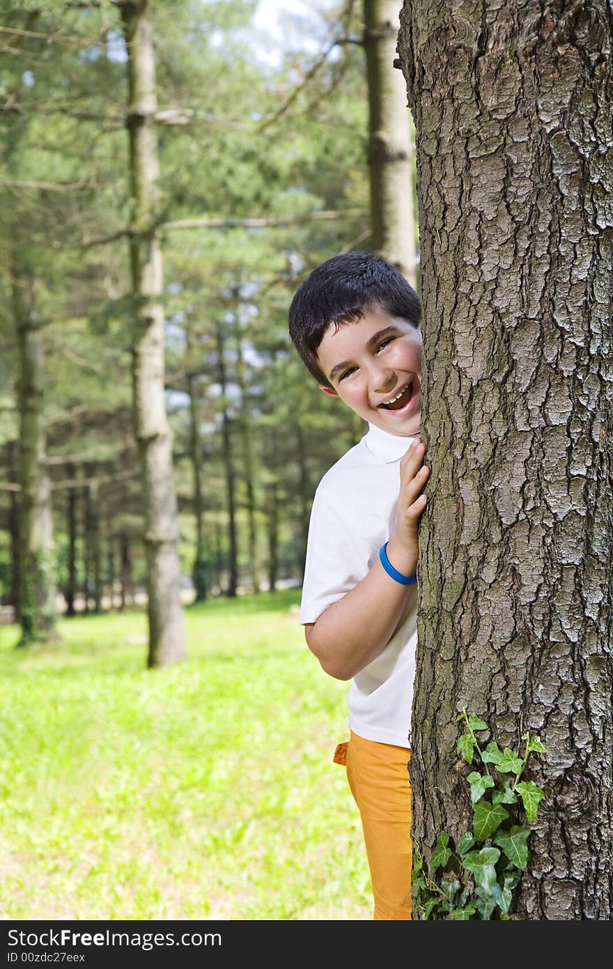 Portrait of young happy boy behind tree at park. Portrait of young happy boy behind tree at park.