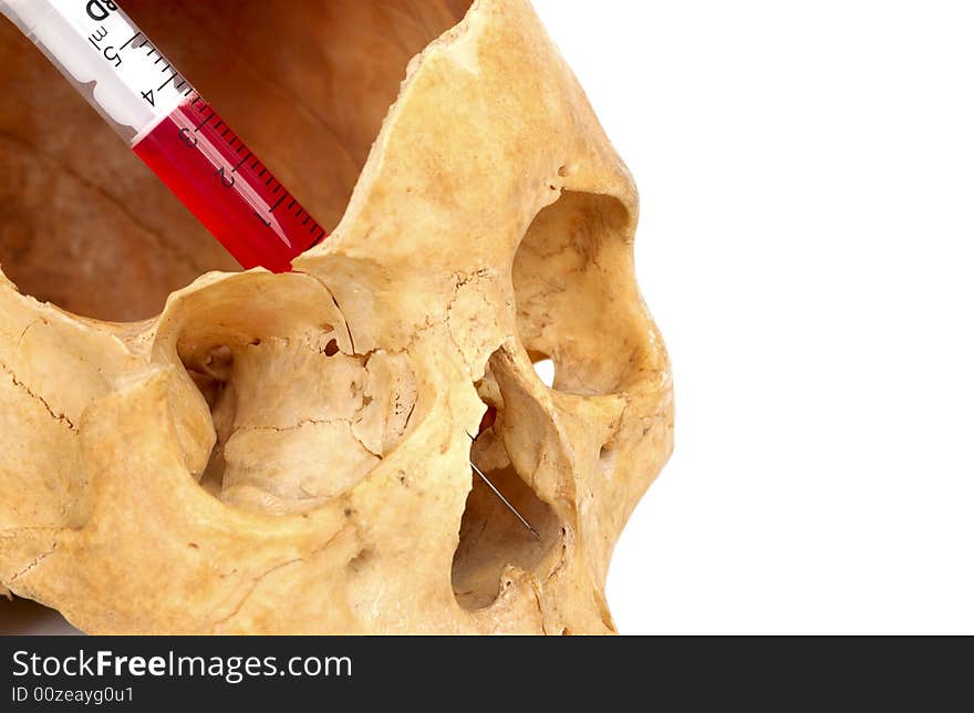 Old broken skull against white background with syringe with red liquid