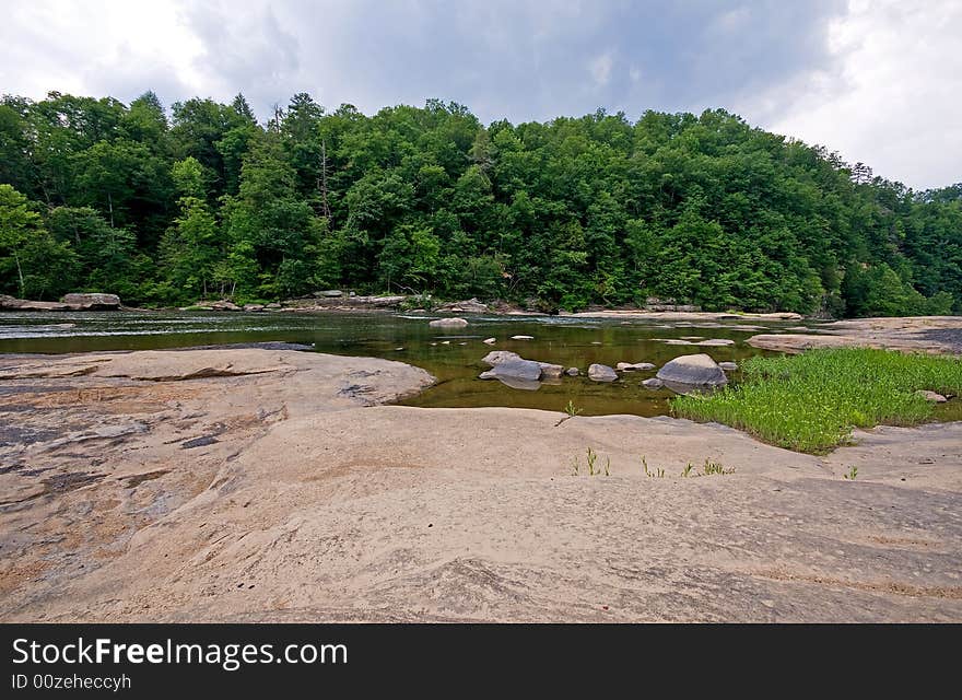 A rocky river shore with woods in the background