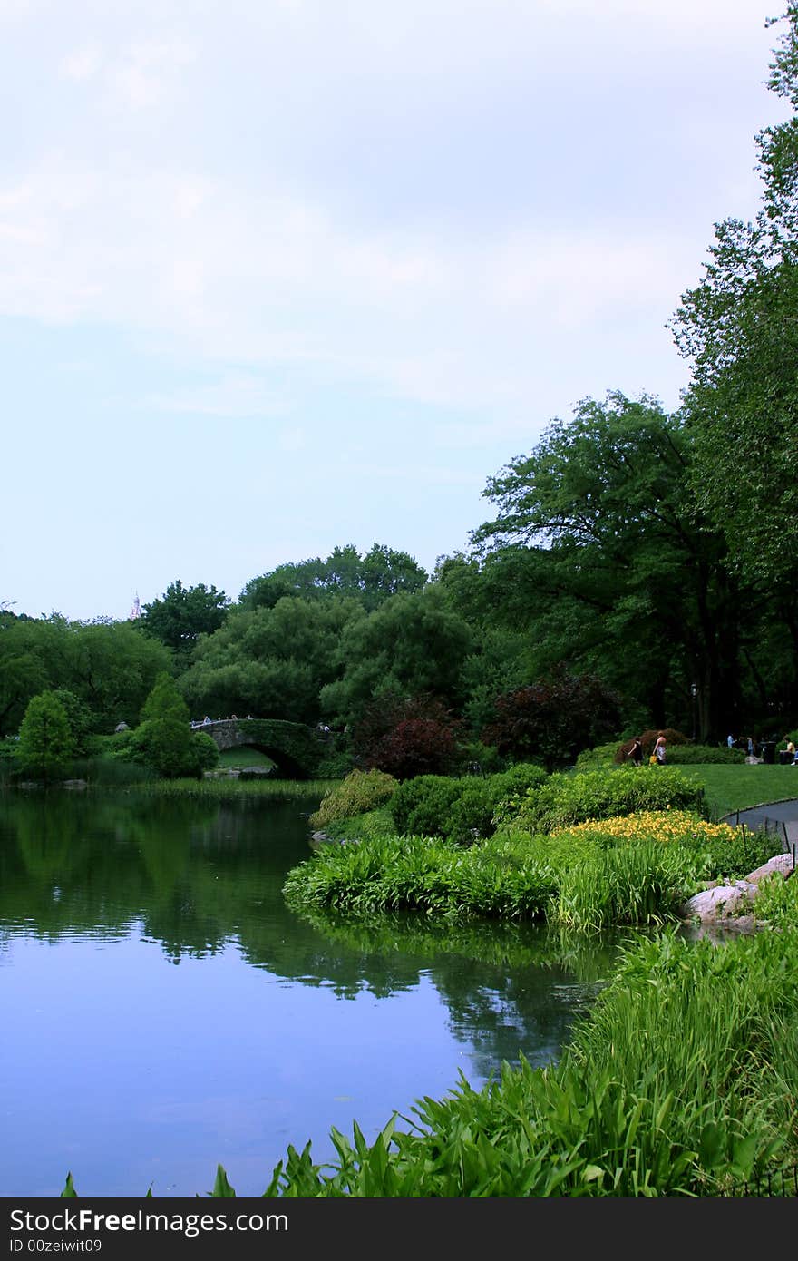 A small bridge crosses over a creek that feeds a large pond inside a park. A small bridge crosses over a creek that feeds a large pond inside a park.