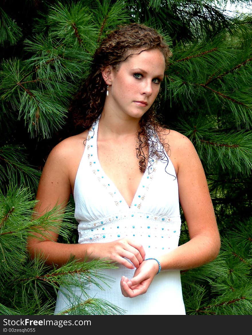 Young woman standing among pine trees in white dress with turquoise trim. Young woman standing among pine trees in white dress with turquoise trim