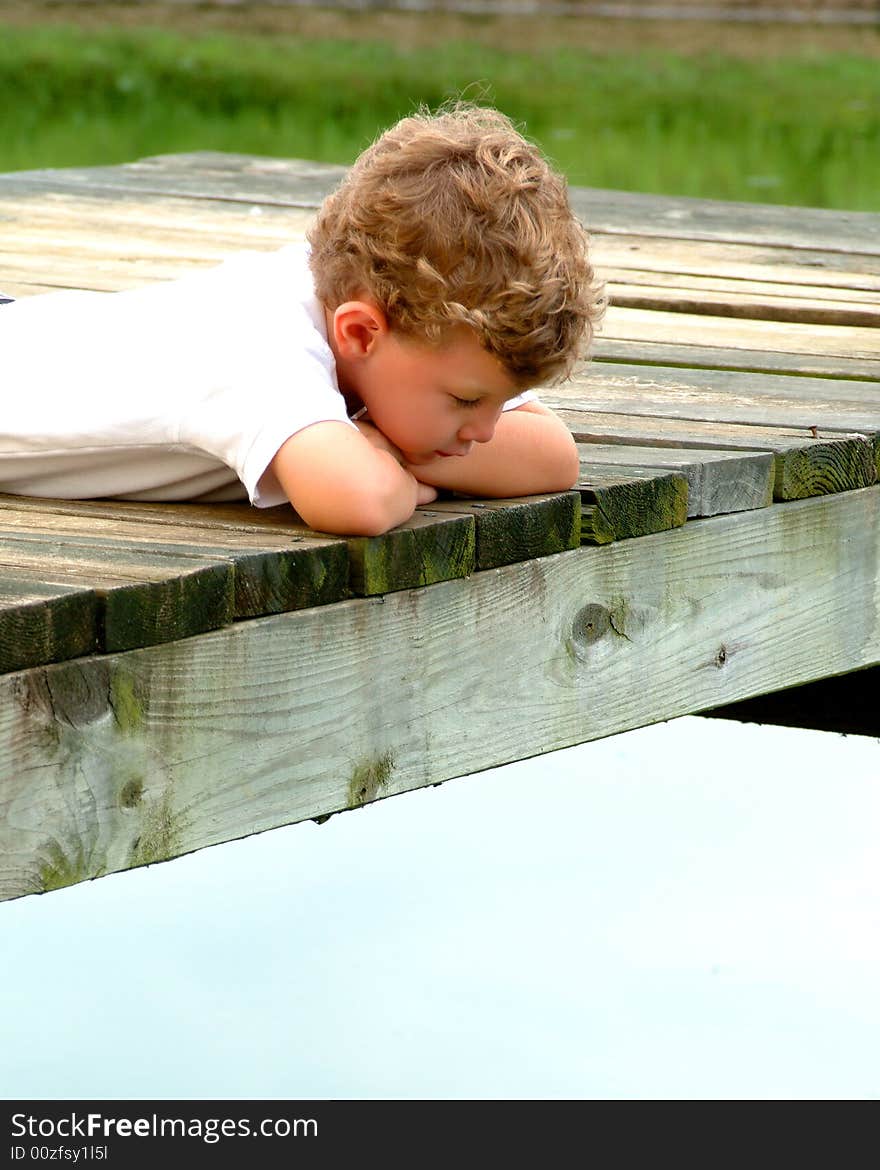 Boy lying on pier looking into water on a cloudy day. Boy lying on pier looking into water on a cloudy day