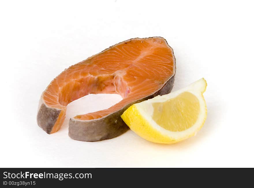 Raw salmon steak and lemon segment on white ground