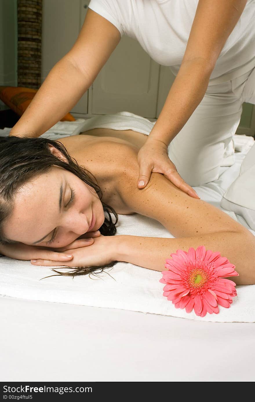 A young girl, with a pink flower near her, gets a massage. She is lying on a white towel. - vertically framed. A young girl, with a pink flower near her, gets a massage. She is lying on a white towel. - vertically framed