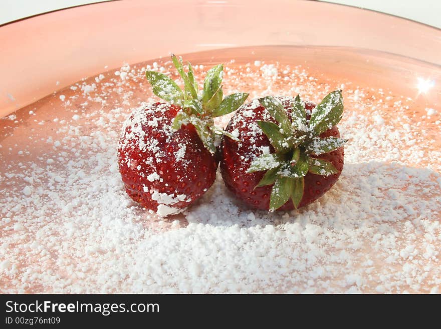 Single strawberry on pink glass plate with powdered sugar on top. Single strawberry on pink glass plate with powdered sugar on top