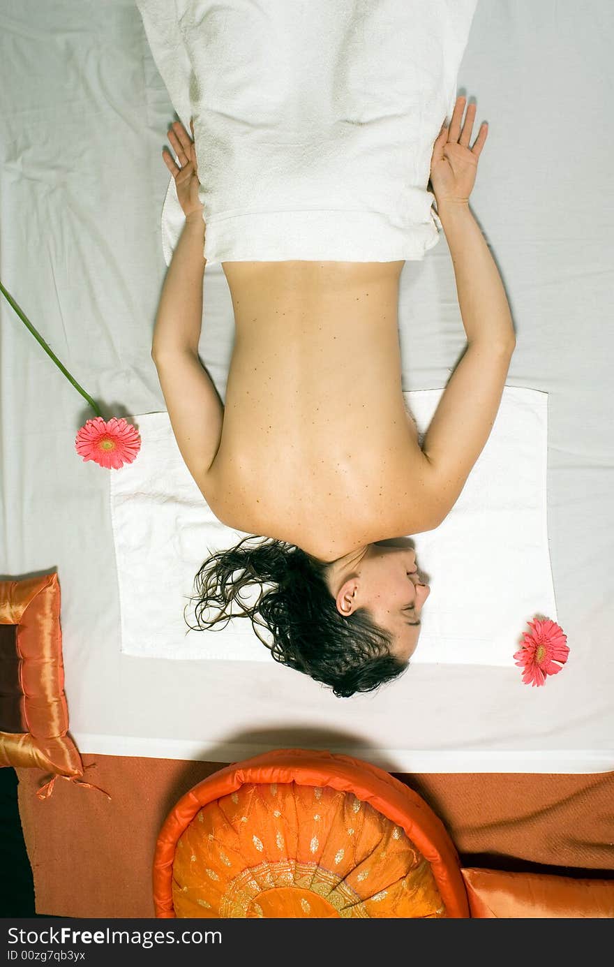 A young girl lying down on a white towel with pink flowers near her. - vertically framed. A young girl lying down on a white towel with pink flowers near her. - vertically framed