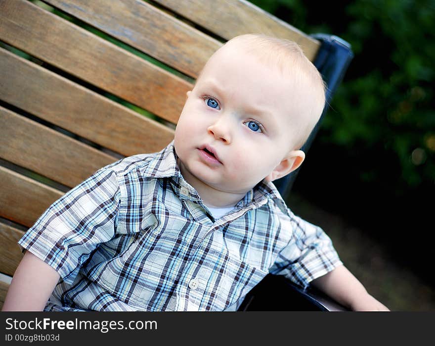 A young child sits on a park bench staring away. - horizontally framed. A young child sits on a park bench staring away. - horizontally framed