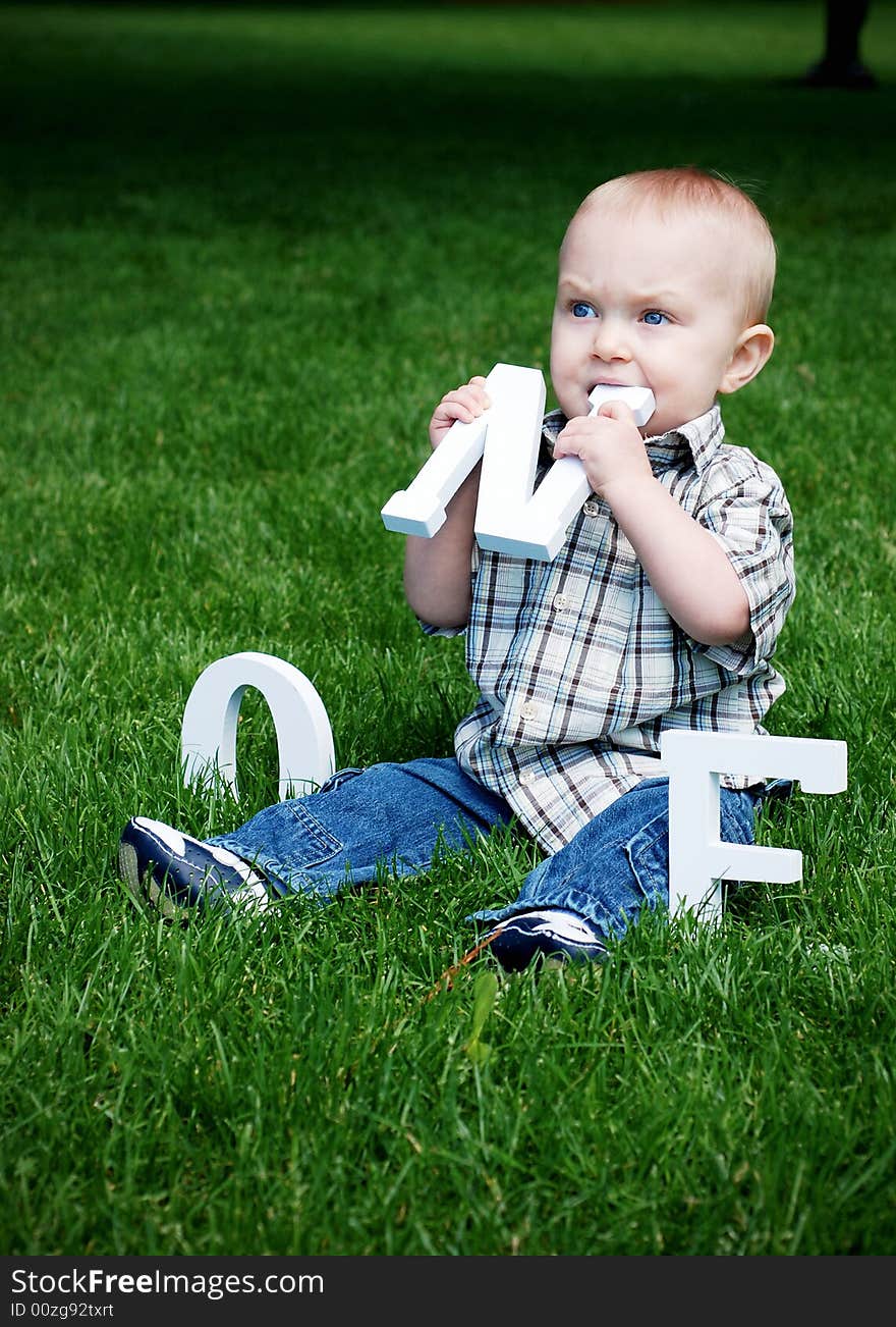 A baby sitting in a field of grass eating a letter N. - vertically framed. A baby sitting in a field of grass eating a letter N. - vertically framed