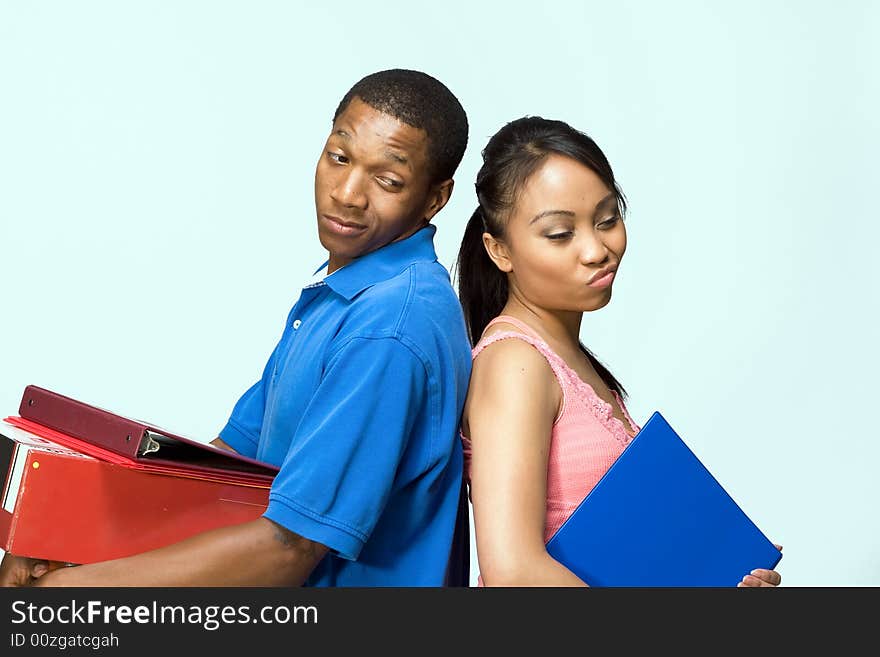 Two students standing back to back carrying books. They look frustrated. Horizontally framed photograph. Two students standing back to back carrying books. They look frustrated. Horizontally framed photograph.