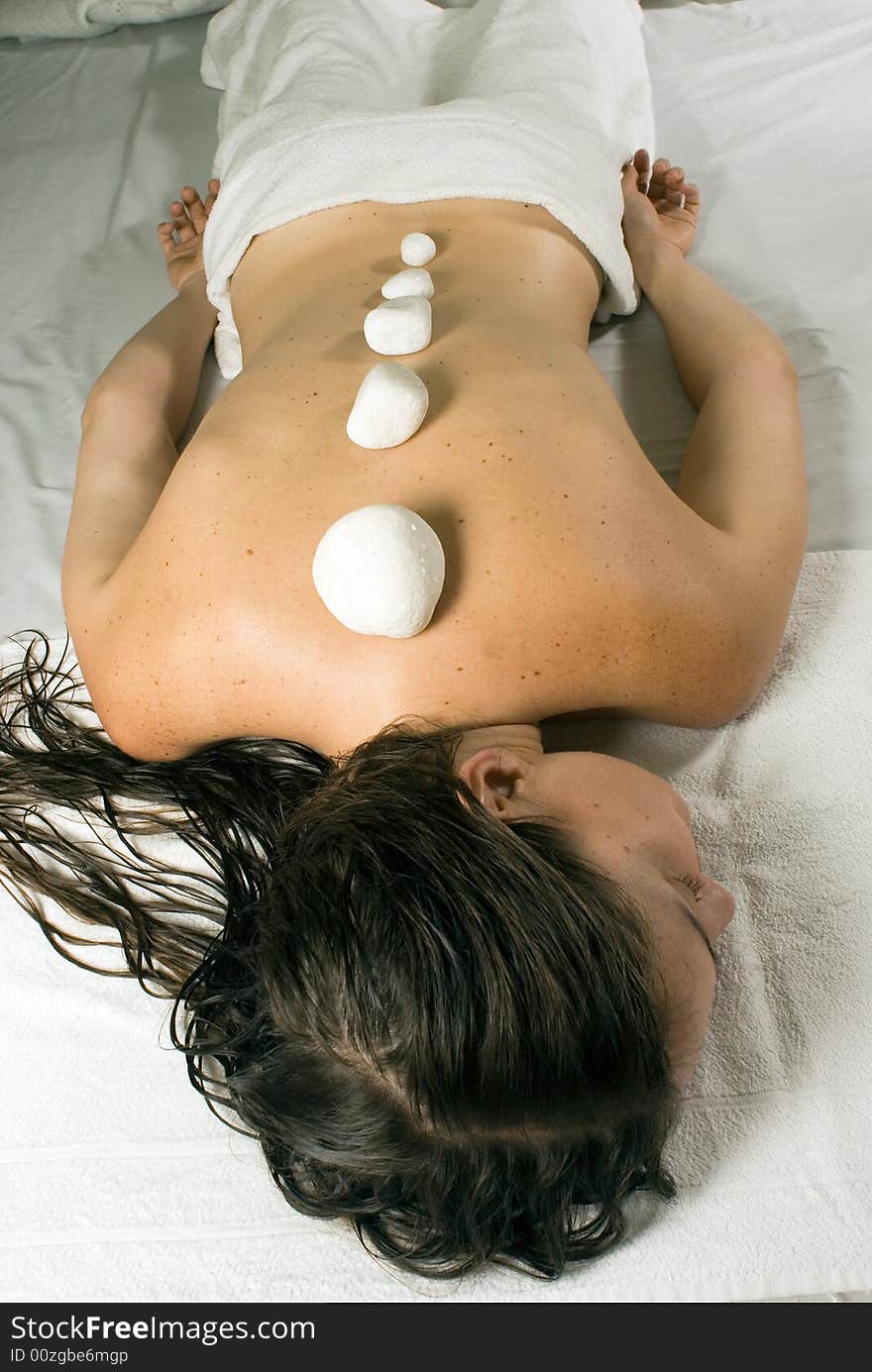 A young girl lying down on a white towel with rocks lining her spine. - vertically framed. A young girl lying down on a white towel with rocks lining her spine. - vertically framed