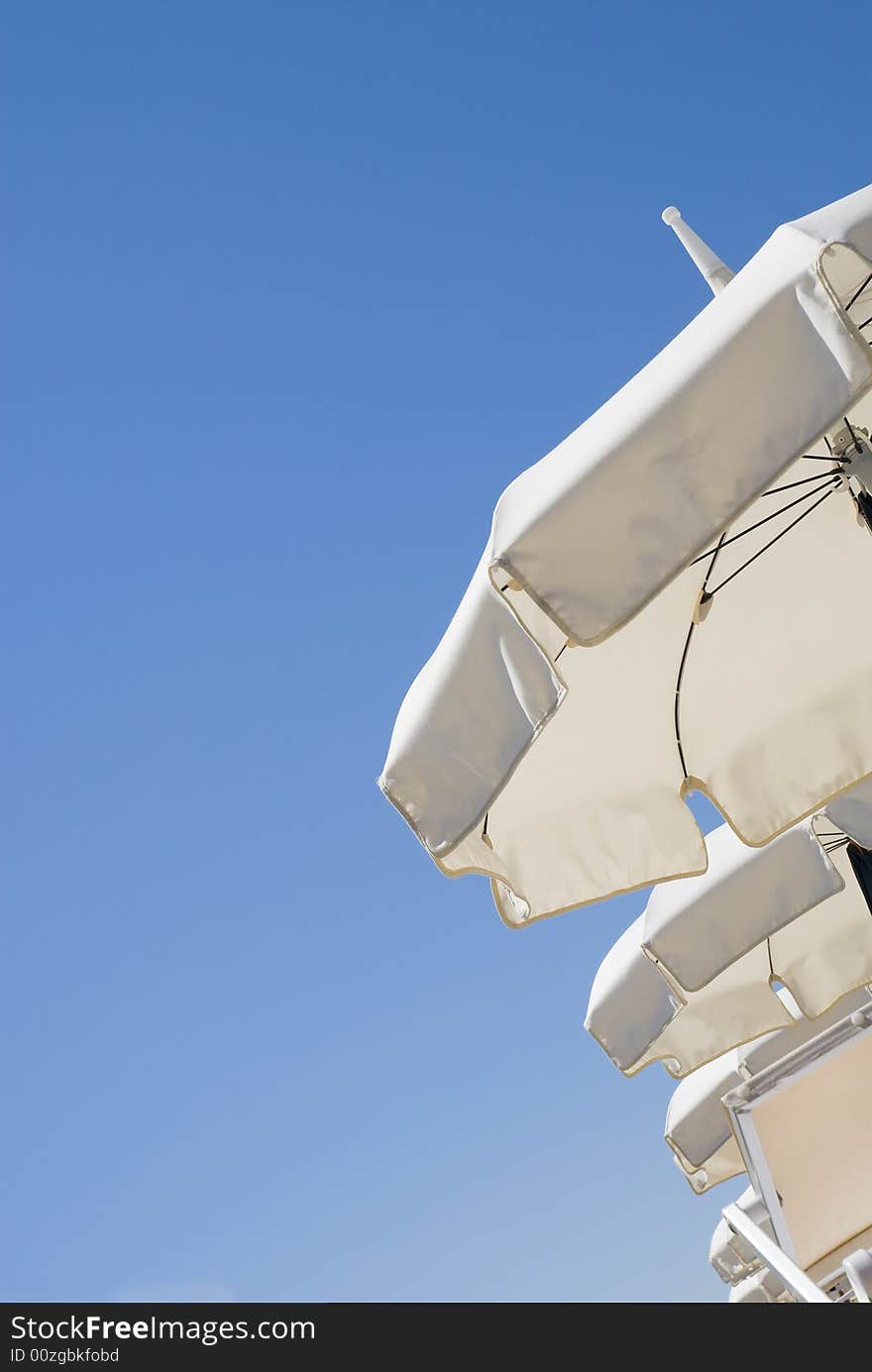 Line of sun white sun umbrellas on a clean blue sky