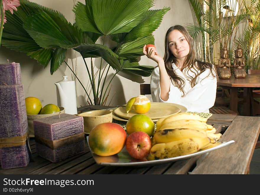 An attractive young girl holding an apple while outdoors, surrounded by fruits and plants. - horizontally framed. An attractive young girl holding an apple while outdoors, surrounded by fruits and plants. - horizontally framed