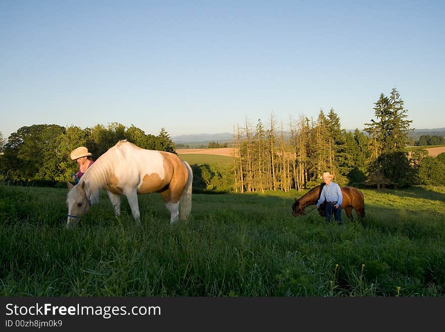 Two farmers walking their horses through grass on a hill. - Horizontally framed. Two farmers walking their horses through grass on a hill. - Horizontally framed