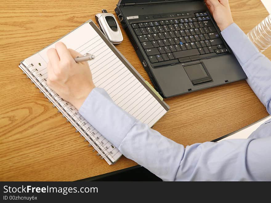 Shot of table with laptop and notepad with hand of woman in casual dress. Shot of table with laptop and notepad with hand of woman in casual dress