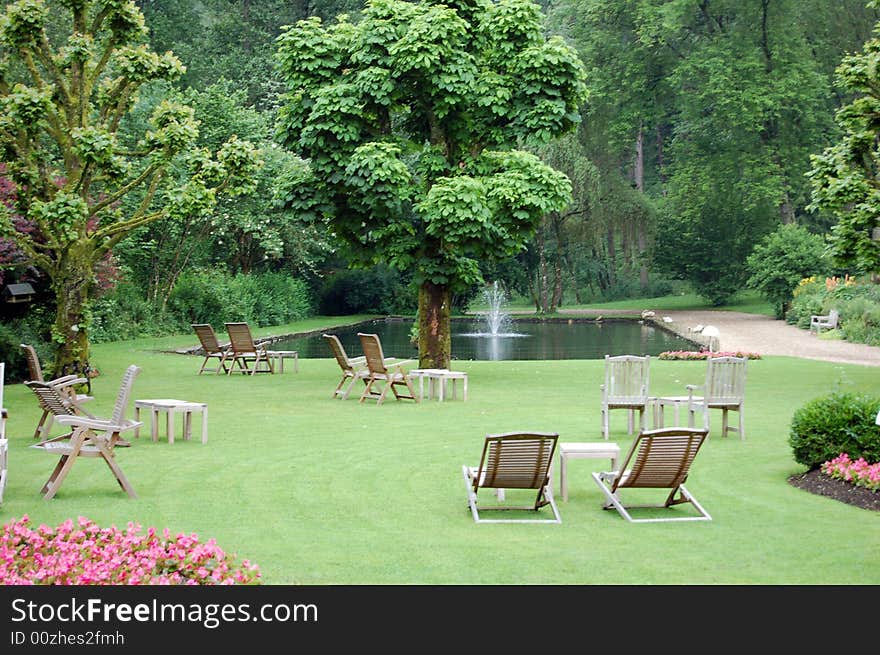 Garden with a small lake and wooden chairs waiting for people looking for a releax. Garden with a small lake and wooden chairs waiting for people looking for a releax