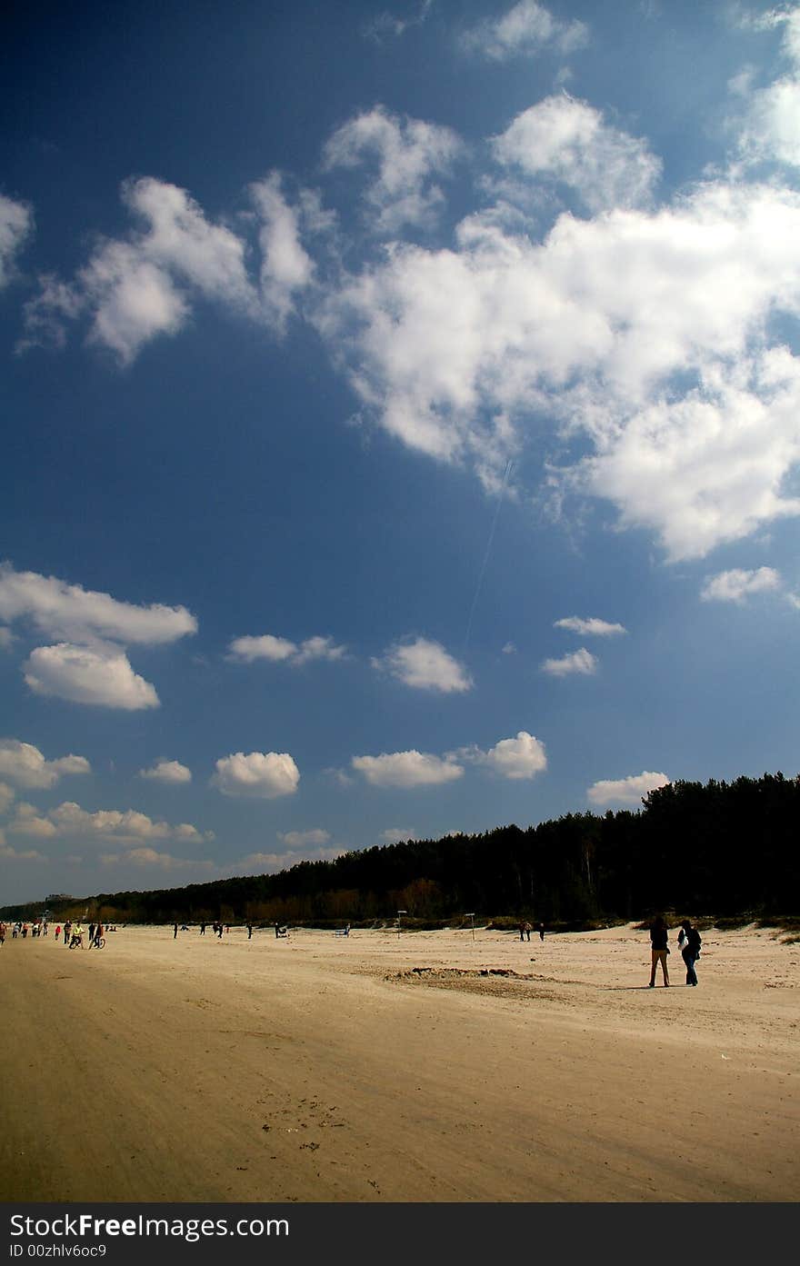 Beach of Riga Gulf with walking people under beautifull clouds in sunny spring day. Beach of Riga Gulf with walking people under beautifull clouds in sunny spring day