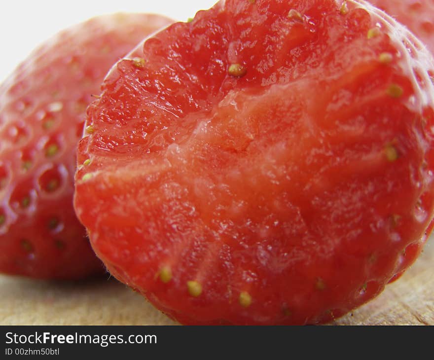 Strawberry macro with a bite, more strawberries in the background, on wooden kitchen board surface against white background, juicy details *RAW format available