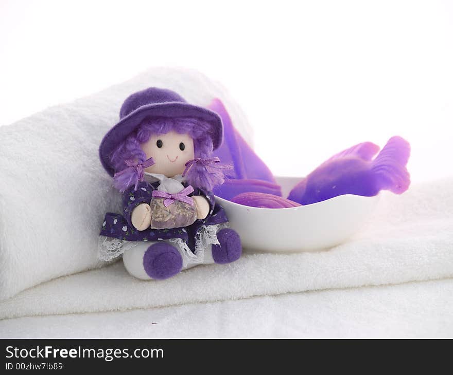 Little rustic doll and lilac soaps laying at white towels, white background. Little rustic doll and lilac soaps laying at white towels, white background