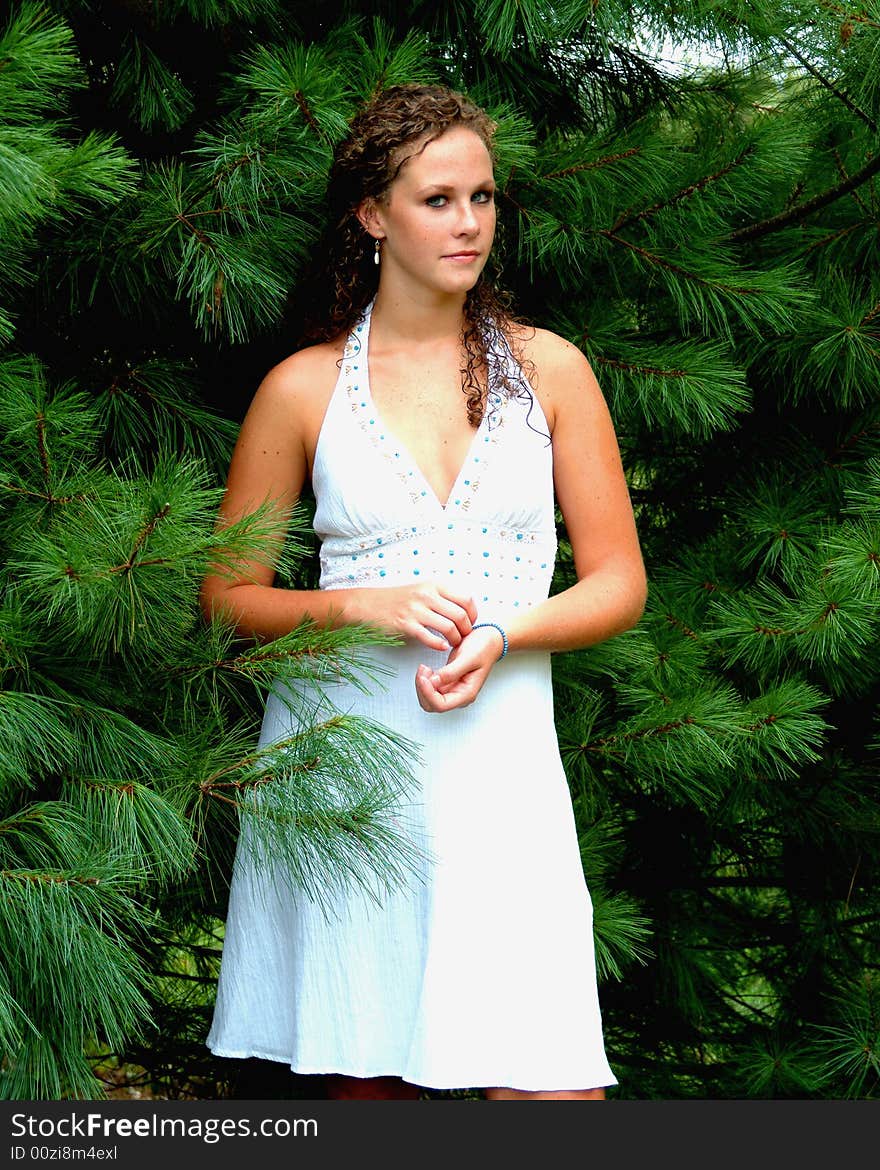 Young woman standing among pine trees in white dress with turquoise trim. Young woman standing among pine trees in white dress with turquoise trim