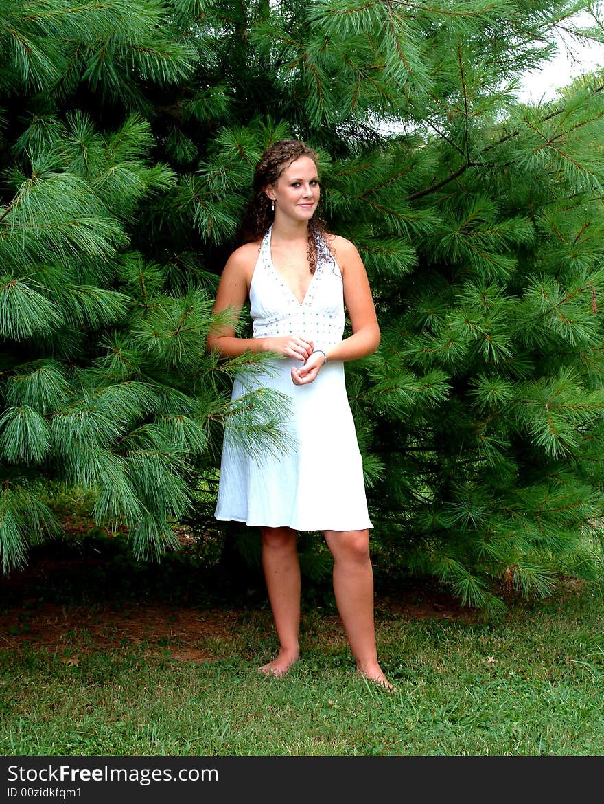 Young woman standing among pine trees in white dress with turquoise trim. Young woman standing among pine trees in white dress with turquoise trim