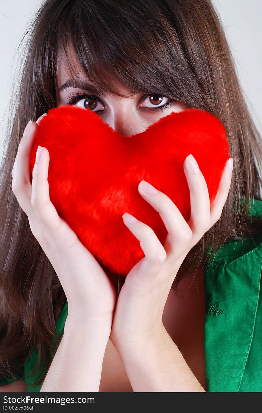 A beautiful girl with a red heart in hands looks a serious look. A beautiful girl with a red heart in hands looks a serious look