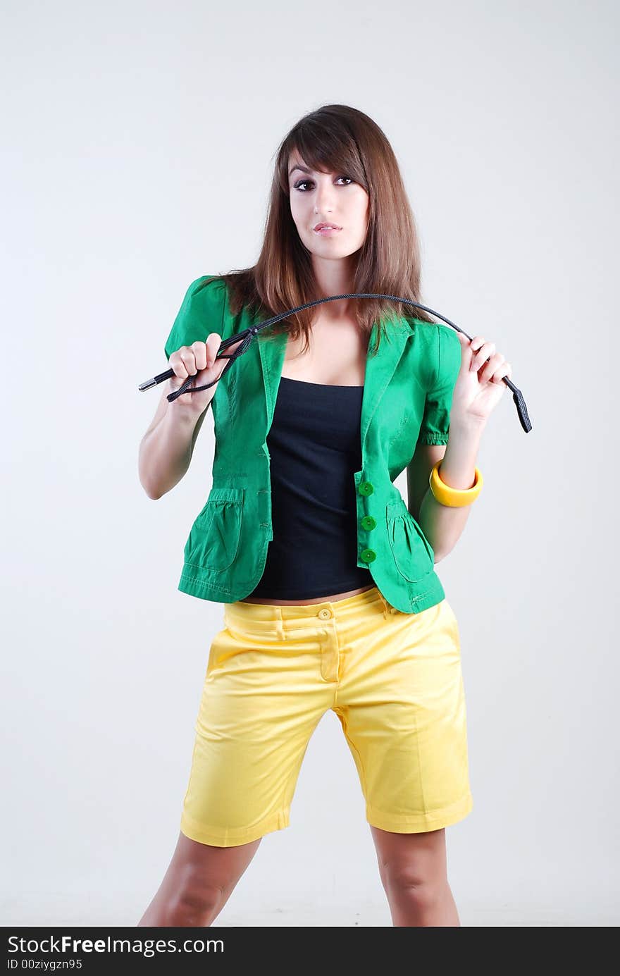 Beautiful girl in a green blouse and yellow shorts with whip on white background. Beautiful girl in a green blouse and yellow shorts with whip on white background