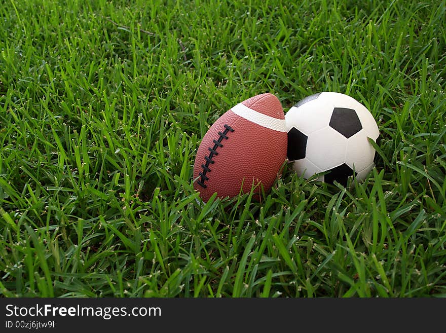 A soccer ball and a football sit next to each other in the grass. A soccer ball and a football sit next to each other in the grass.