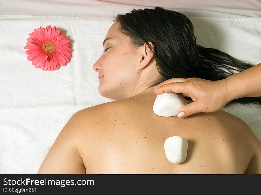 A girl getting a white rock placed on her back. A pink flower is near her as she lies on her white towel. - horizontally framed. A girl getting a white rock placed on her back. A pink flower is near her as she lies on her white towel. - horizontally framed