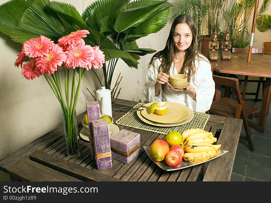 A young girl outside surrounded by plants, fruits, and flowers, holding a cup, smiling for the camera. - horizontally framed. A young girl outside surrounded by plants, fruits, and flowers, holding a cup, smiling for the camera. - horizontally framed