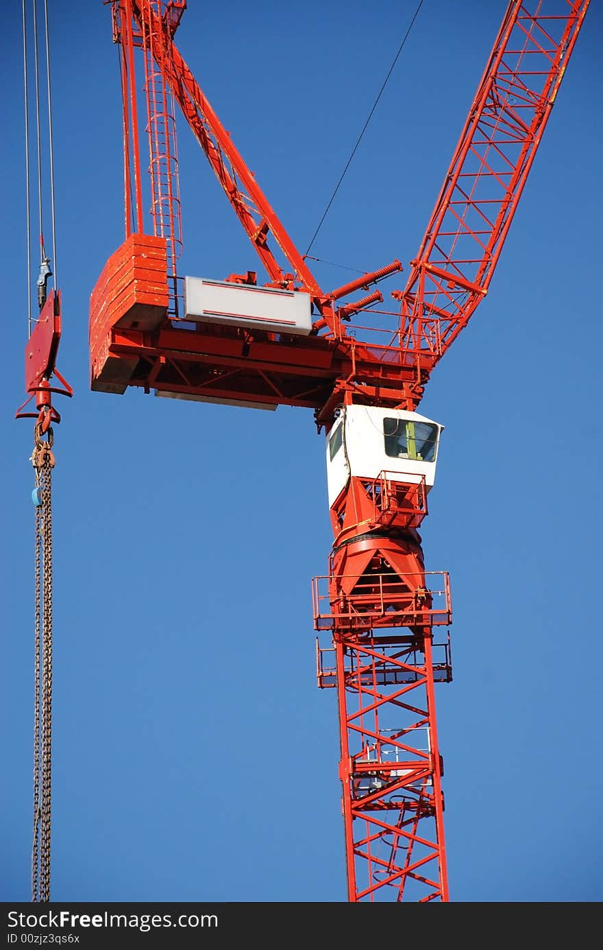 A red tower crane undertaking construction work, against a blue sky. A red tower crane undertaking construction work, against a blue sky