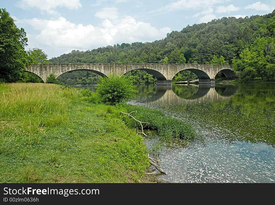 A stone arched bridge in a woody setting