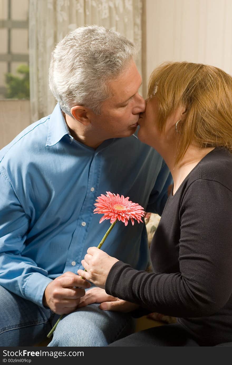 Romantic couple kissing on a couch, holding a bright flower. vertically framed shot. Romantic couple kissing on a couch, holding a bright flower. vertically framed shot.