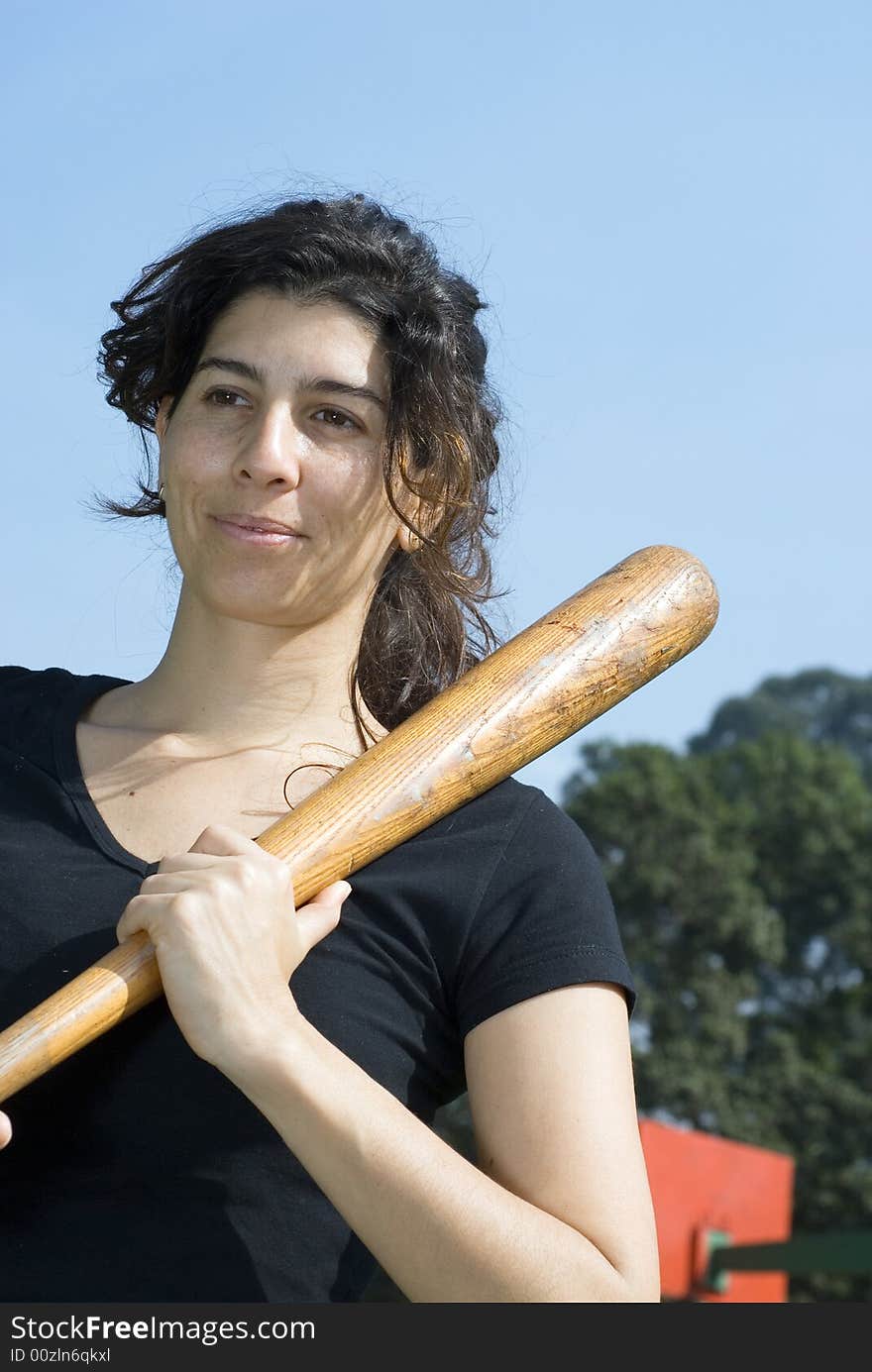 A smiling woman in a park is holding a baseball bat.  Vertically framed shot. A smiling woman in a park is holding a baseball bat.  Vertically framed shot.