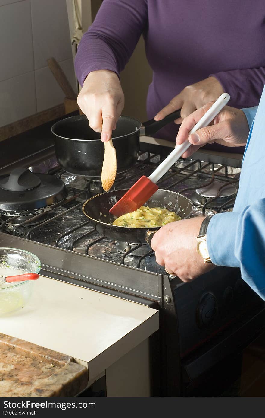 A couple make scrambled eggs over the stove, together. - vertically framed. A couple make scrambled eggs over the stove, together. - vertically framed