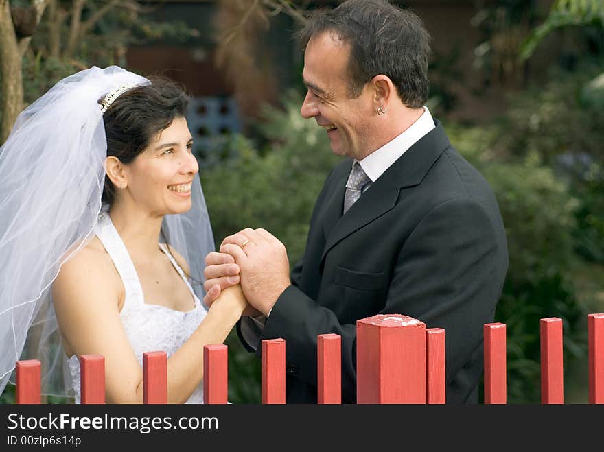 A newly married couple, stare at each other behind a red gate, holding hands and smiling. - horizontally framed. A newly married couple, stare at each other behind a red gate, holding hands and smiling. - horizontally framed