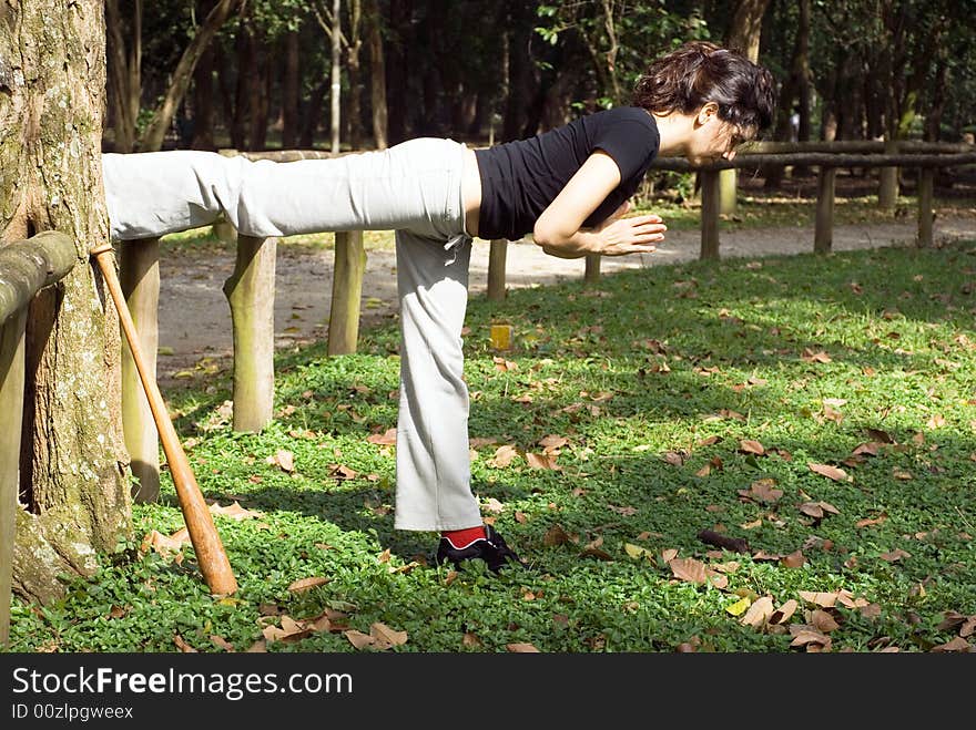 A woman is standing in a yoga pose next to a tree.  She is stretching her muscles.  A baseball bat is leaning against the tree.  Horizontally framed photo. A woman is standing in a yoga pose next to a tree.  She is stretching her muscles.  A baseball bat is leaning against the tree.  Horizontally framed photo.