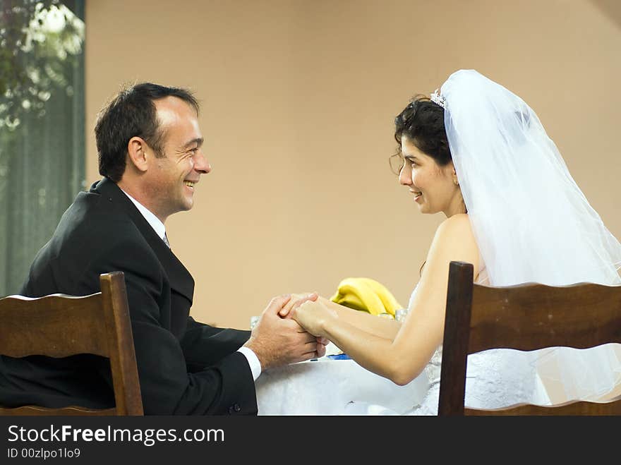 A couple of newly weds, sit at a table, with bananas on it, holding hands, smiling at each other. - horizontally framed. A couple of newly weds, sit at a table, with bananas on it, holding hands, smiling at each other. - horizontally framed