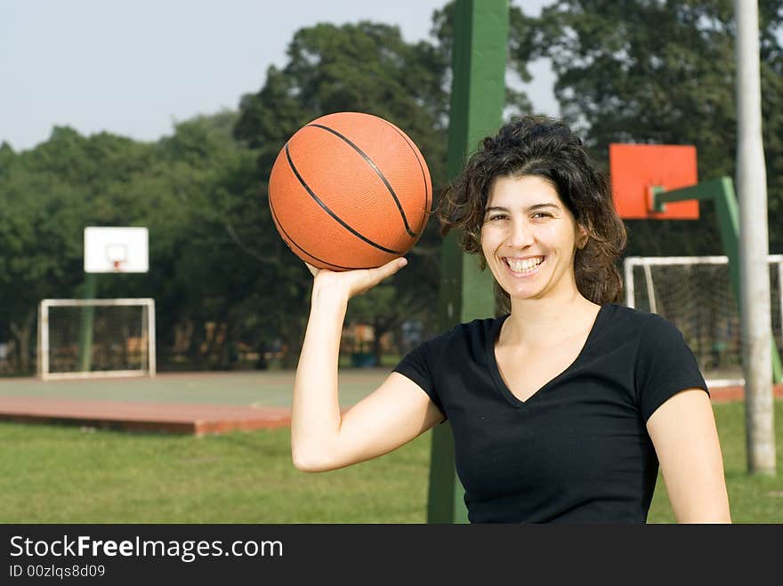 A woman smiling for the camera with a basketball court in the background, holding a basketball in one hand. - horizontally framed. A woman smiling for the camera with a basketball court in the background, holding a basketball in one hand. - horizontally framed