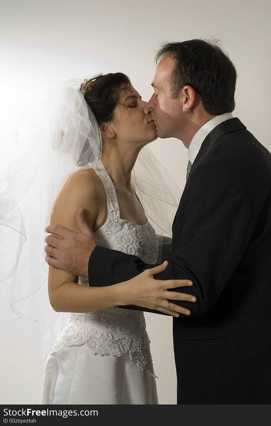 A couple of newlyweds kiss, while still in their wedding outfits. - vertically framed. A couple of newlyweds kiss, while still in their wedding outfits. - vertically framed