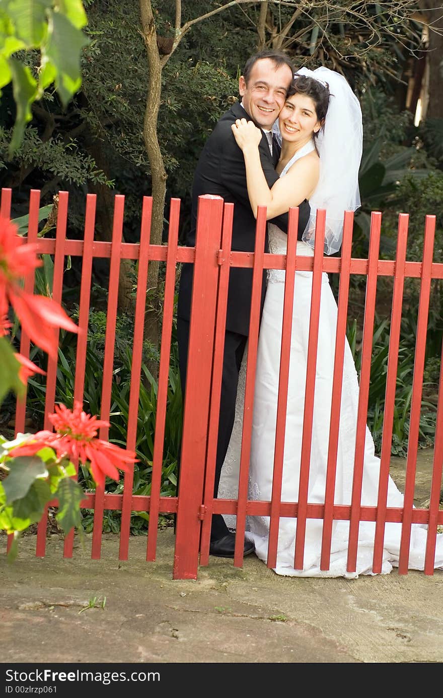 A couple, newly married, smile for the camera while hugging behind a red gate. - vertically framed. A couple, newly married, smile for the camera while hugging behind a red gate. - vertically framed