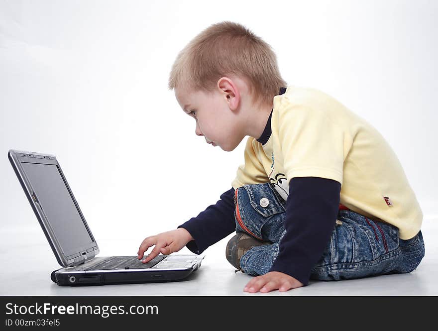 The little boy sits a feather the laptop and attentively looks. The little boy sits a feather the laptop and attentively looks