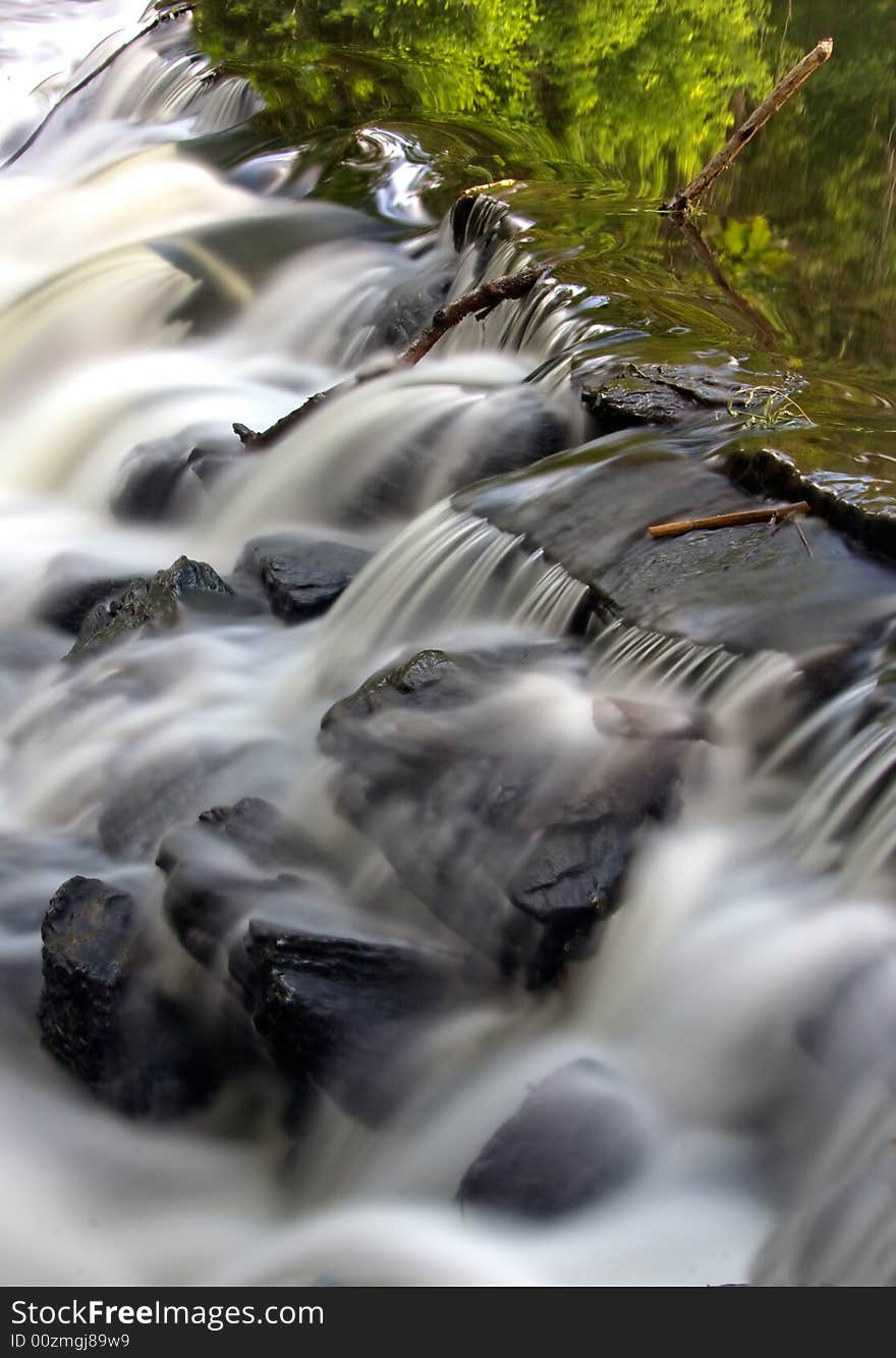 Shot if cascading water over rocks with tree reflections. Shot if cascading water over rocks with tree reflections