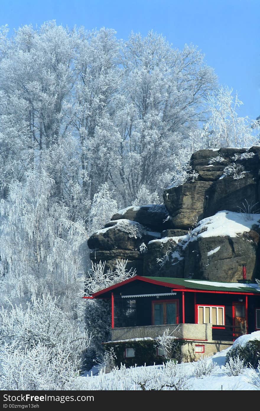 Romantic  snowy scenery cottage below rock