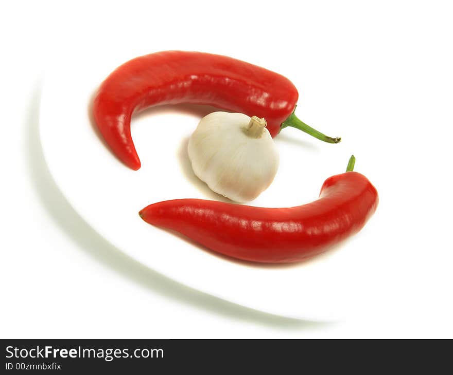 Two fresh chili peppers and a bulb of garlic on a white plate and isolated on white background. Two fresh chili peppers and a bulb of garlic on a white plate and isolated on white background