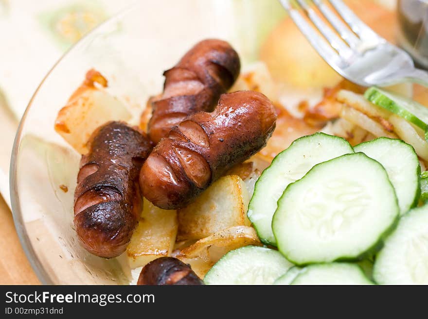 Sausages, potato and cucumber on a glass plate. Sausages, potato and cucumber on a glass plate