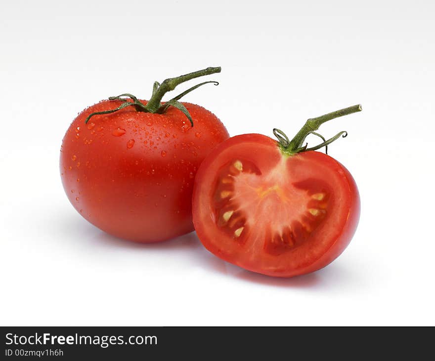 An arrangement of a whole Tomato and a half on a white background with water droplets and stalks. An arrangement of a whole Tomato and a half on a white background with water droplets and stalks.