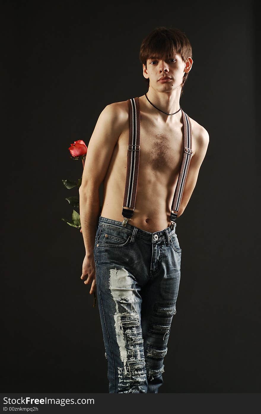 short haired man with a nude torso wearing jeans hides a red rose behind his back. short haired man with a nude torso wearing jeans hides a red rose behind his back