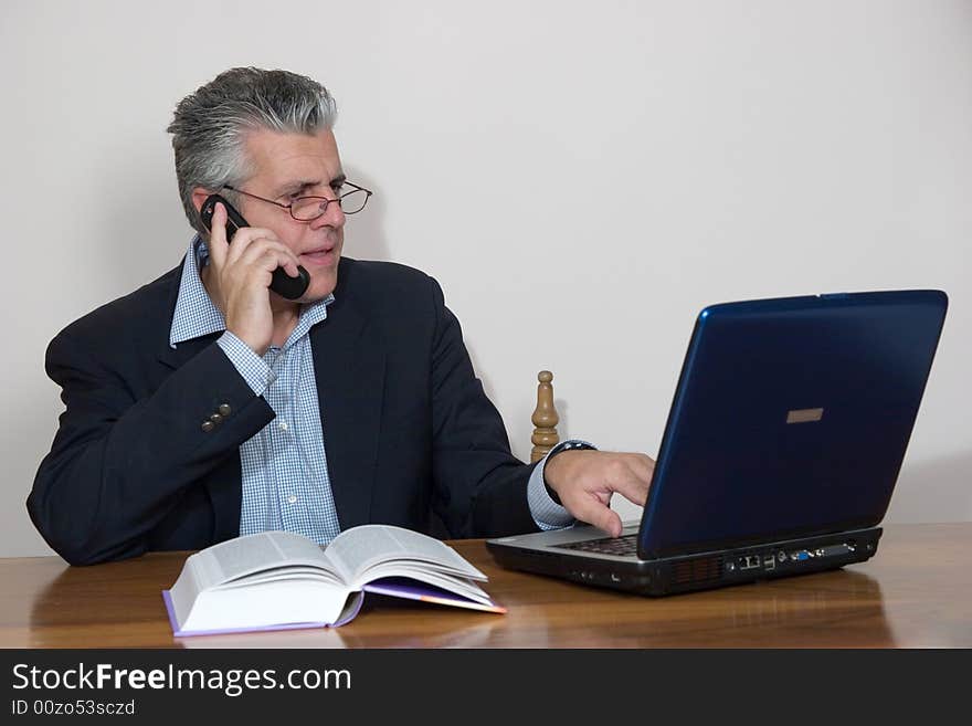 A businessman working in his study with a computer and a mobile. A businessman working in his study with a computer and a mobile